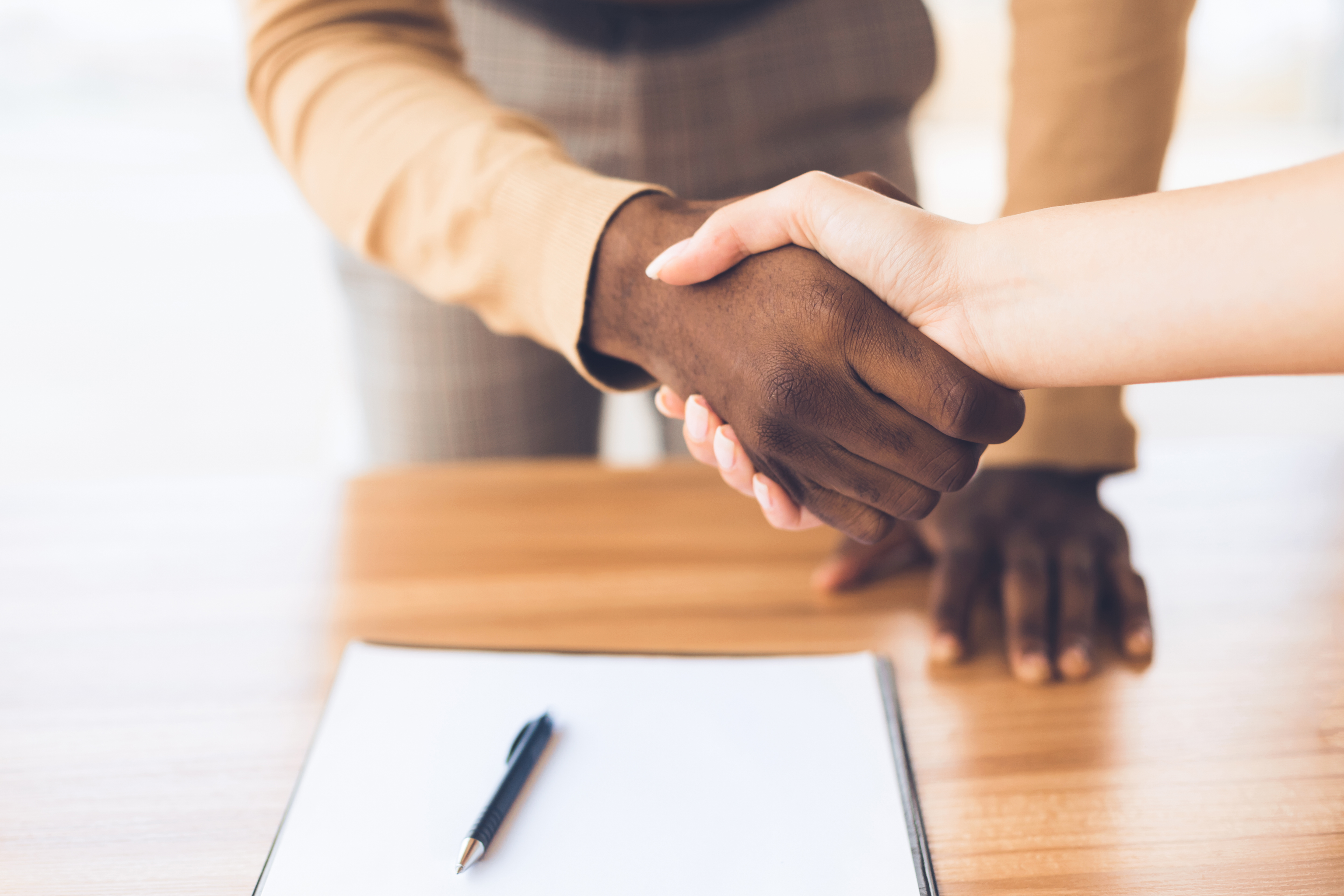 Man shaking hands with another person, leaning over a table